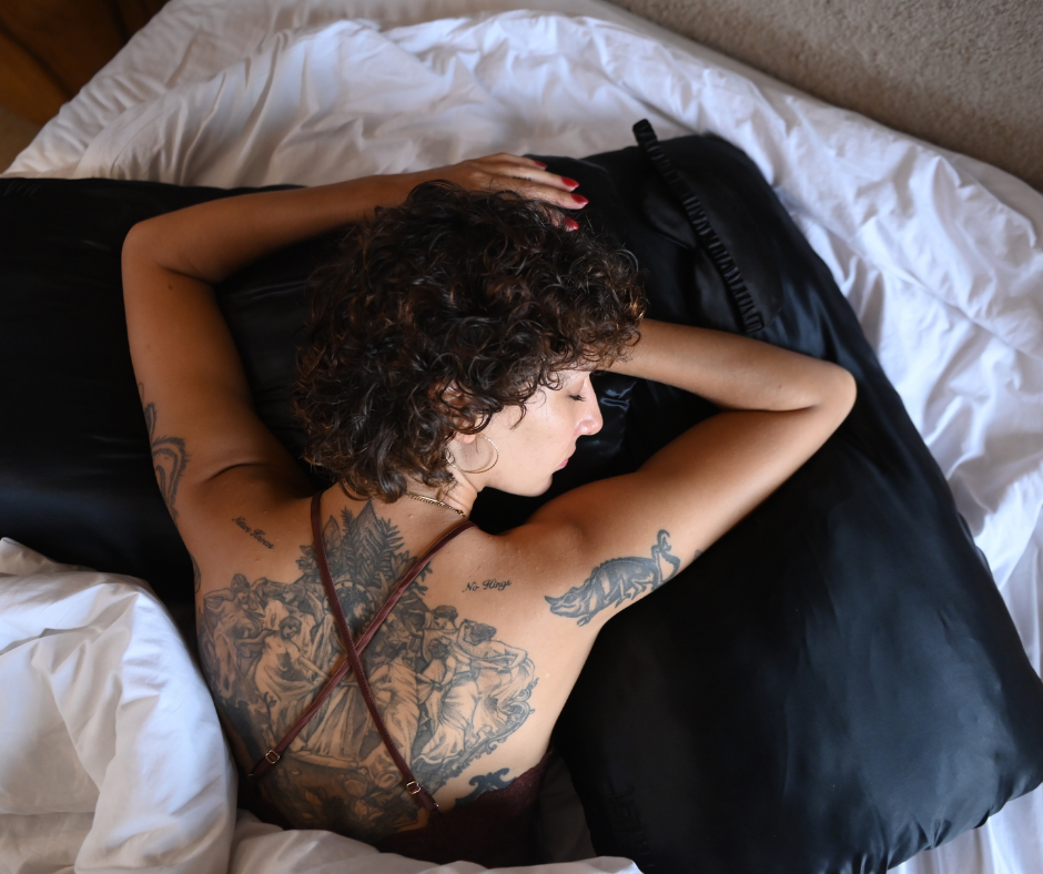 Woman with tattoos lying on a bed with black ONYX PillowWraps Mulberry silk pillowcase.