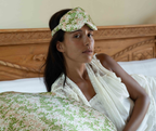 Woman wearing a floral eye mask and white robe in bed with LATRAVLA