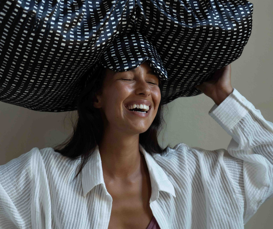 Woman holding a large black and white checkered pillowwrap and pillowmask on her head with a neutral background