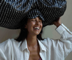 Woman holding a large black and white checkered pillowwrap and pillowmask on her head with a neutral background