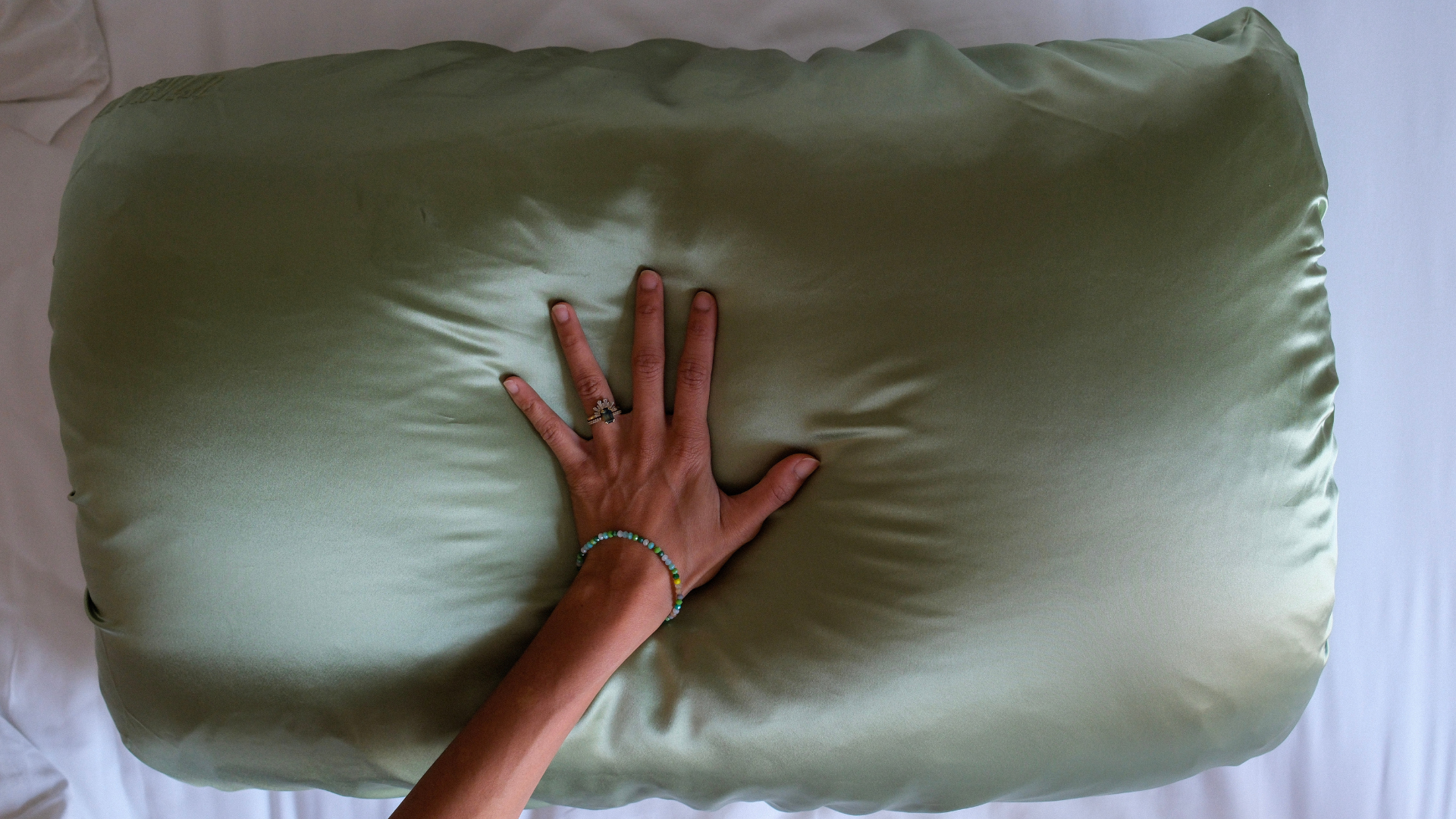 Hand resting on a green latravla mulberry silk pillow against a hotel bed.