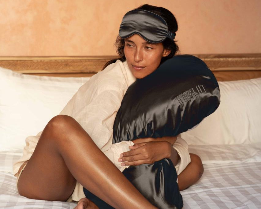 Model on a hotel bed holding the worlds first 100% mulberry silk and silver nanoparticle infused travel pillowcase.